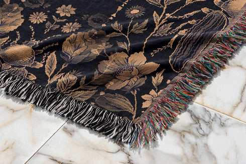 Black cotton throw blanket featuring woven bronze beetles and botanical motifs with multicolored fringe trim.